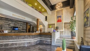 A reception area with a marble floor, a reception desk, a chandelier, and a staircase leading to an upper level. - Hotel Lirak (Tetovo)