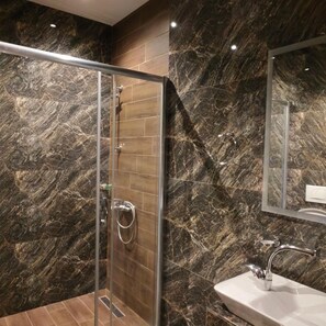 A modern bathroom with a glass-enclosed shower, a marble-tiled wall, and a white sink with a chrome faucet.