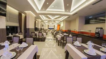 A hotel dining area with tables set for guests, a buffet line, and a modern ceiling design.