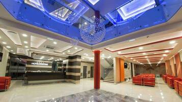 A hotel lobby with a reception desk, a staircase, and a seating area.