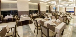 Un vaste espace dédié à la salle à manger, avec de nombreuses tables dressées, de grandes fenêtres et un design moderne au niveau du plafond.