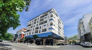Ett hotell med flera våningar och modern design, med balkonger på varje våningsplan, en restaurang på markplan och en parkeringsplats.