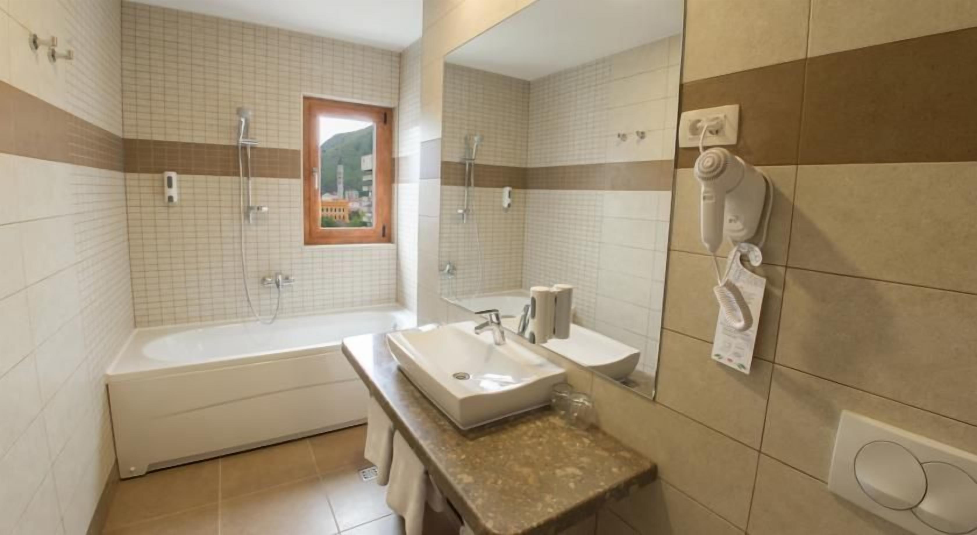 A bathroom with a bathtub, a sink, a mirror, and a window.