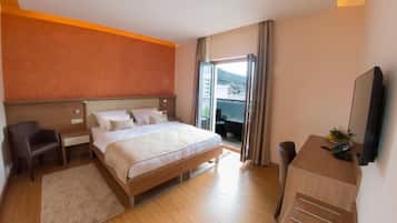A hotel room with a bed, a desk, a chair, a TV, and a window with curtains.