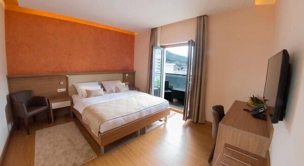 A hotel room with a bed, a desk, a chair, a TV, and a window with curtains.