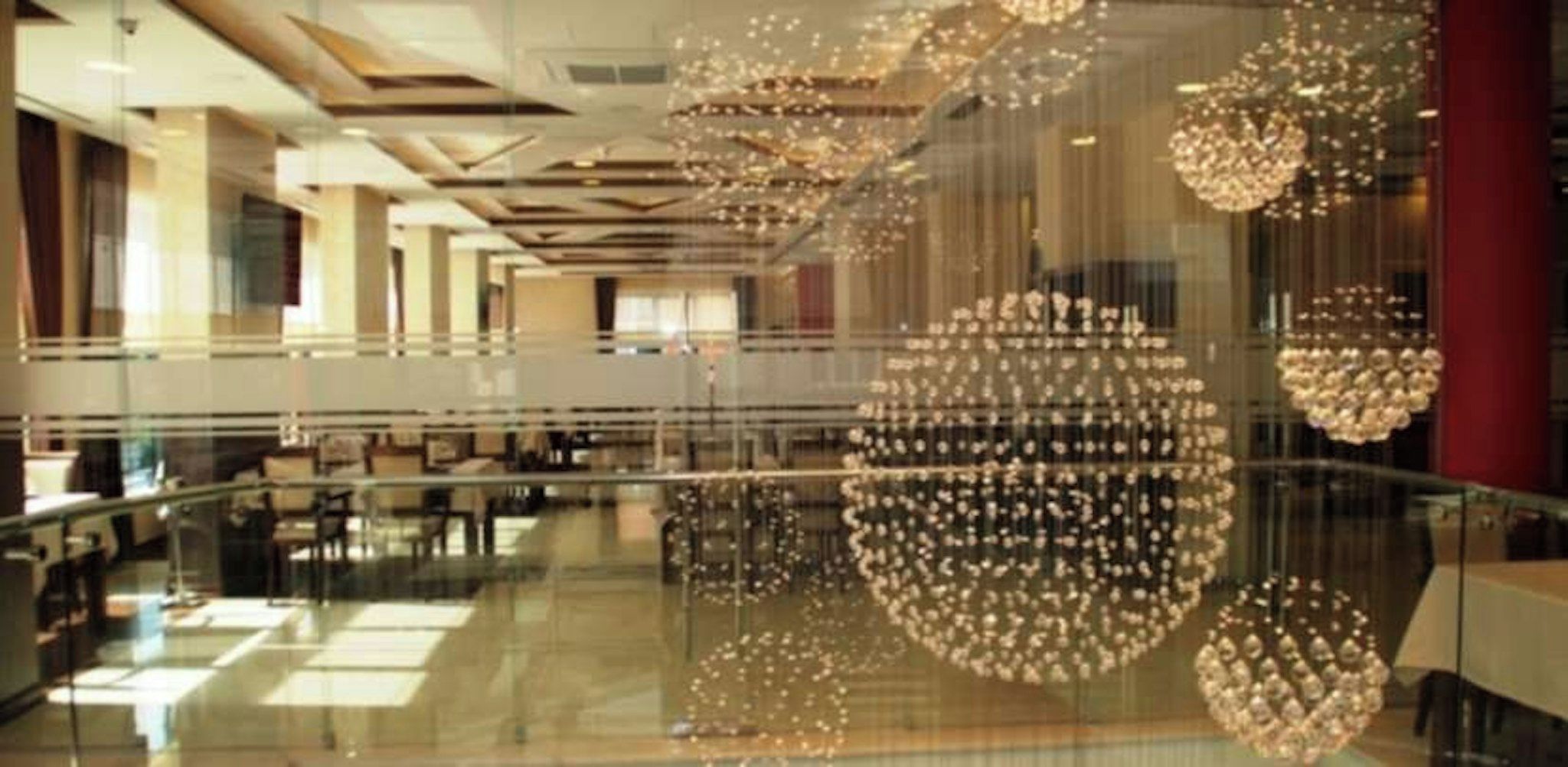 A spacious lobby with a glass floor, allowing views of the lower level, and multiple spherical chandeliers hanging from the ceiling.