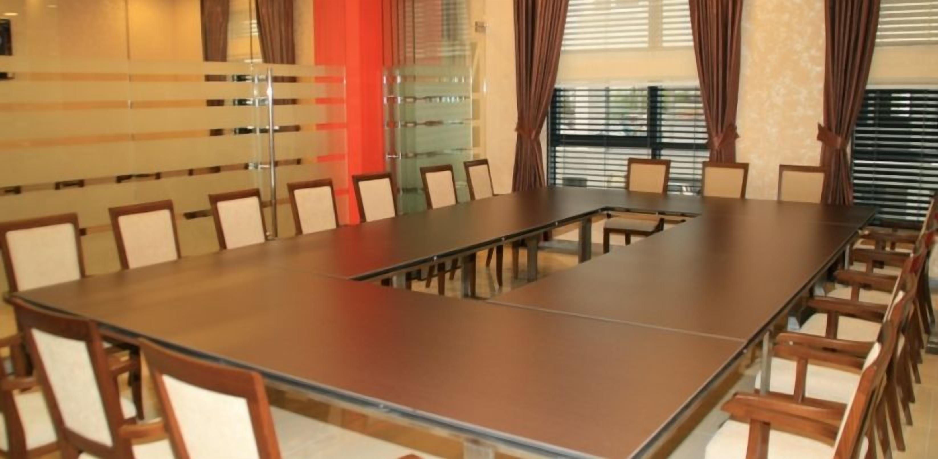A conference room with a long table and chairs, a glass partition, and windows with curtains.