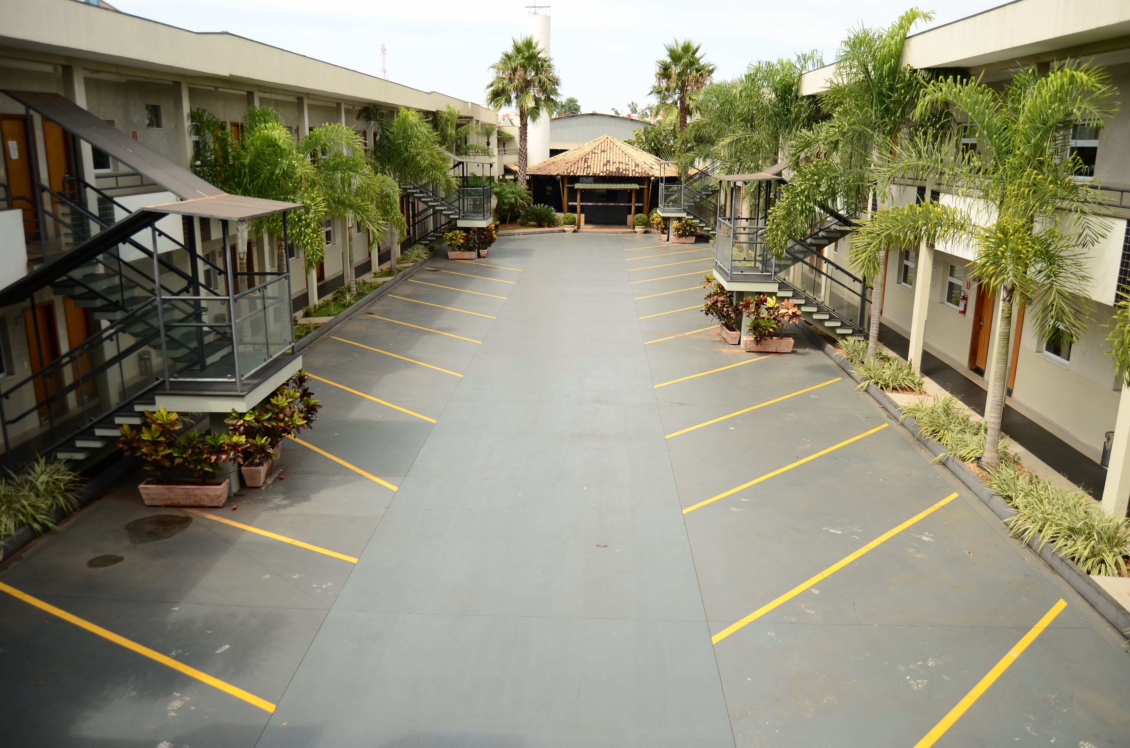 Un patio de hotel con un espacio abierto central, rodeado por varios pisos de habitaciones, palmeras y plantas en macetas.