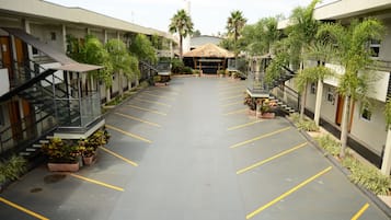 Un patio de hotel con un espacio abierto central, rodeado por varios pisos de habitaciones, palmeras y plantas en macetas.