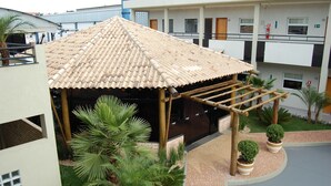 Un espace extérieur abrité, doté d’un toit en tuiles, entouré de verdure et bordé d’un bâtiment avec de nombreuses fenêtres et des balcons.