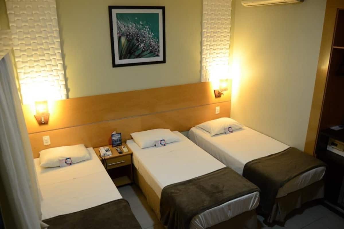 Ein Hotelzimmer mit drei Einzelbetten, einem Nachttisch mit Telefon und Lampe sowie einem Gemälde an der Wand.