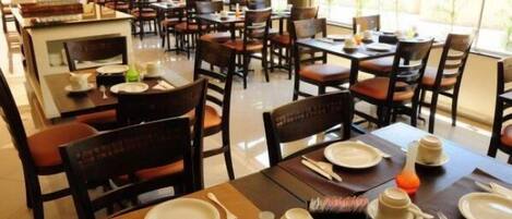 A restaurant with multiple tables and chairs, some with plates and cutlery set.