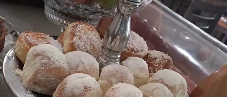 A buffet table with various dishes including a plate of pastries dusted with powdered sugar, a bowl of fruits, and a decorative silver salt shaker.