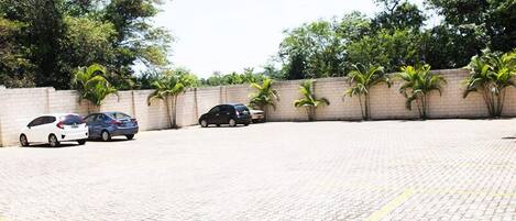 A paved parking area with cars parked, surrounded by a brick wall and palm trees.
