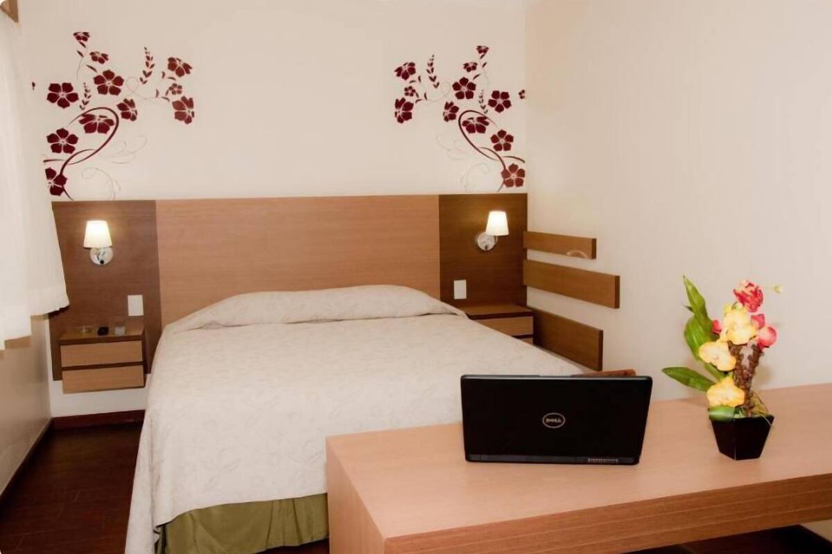 A hotel room with a bed, a desk with a laptop, bedside lamps, and a wall with floral decorations.
