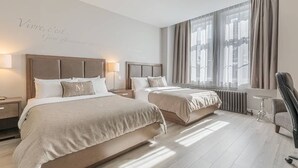 Una habitación de hotel con dos camas, un ventanal con cortinas, una silla y una mesita de noche.