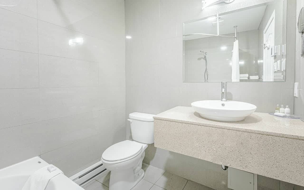 Un bagno moderno con un water bianco, un lavabo a colonna e un grande specchio sopra il mobile.