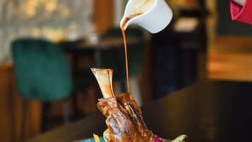Une personne verse de la sauce sur un plat contenant un morceau de viande avec un os et des légumes.