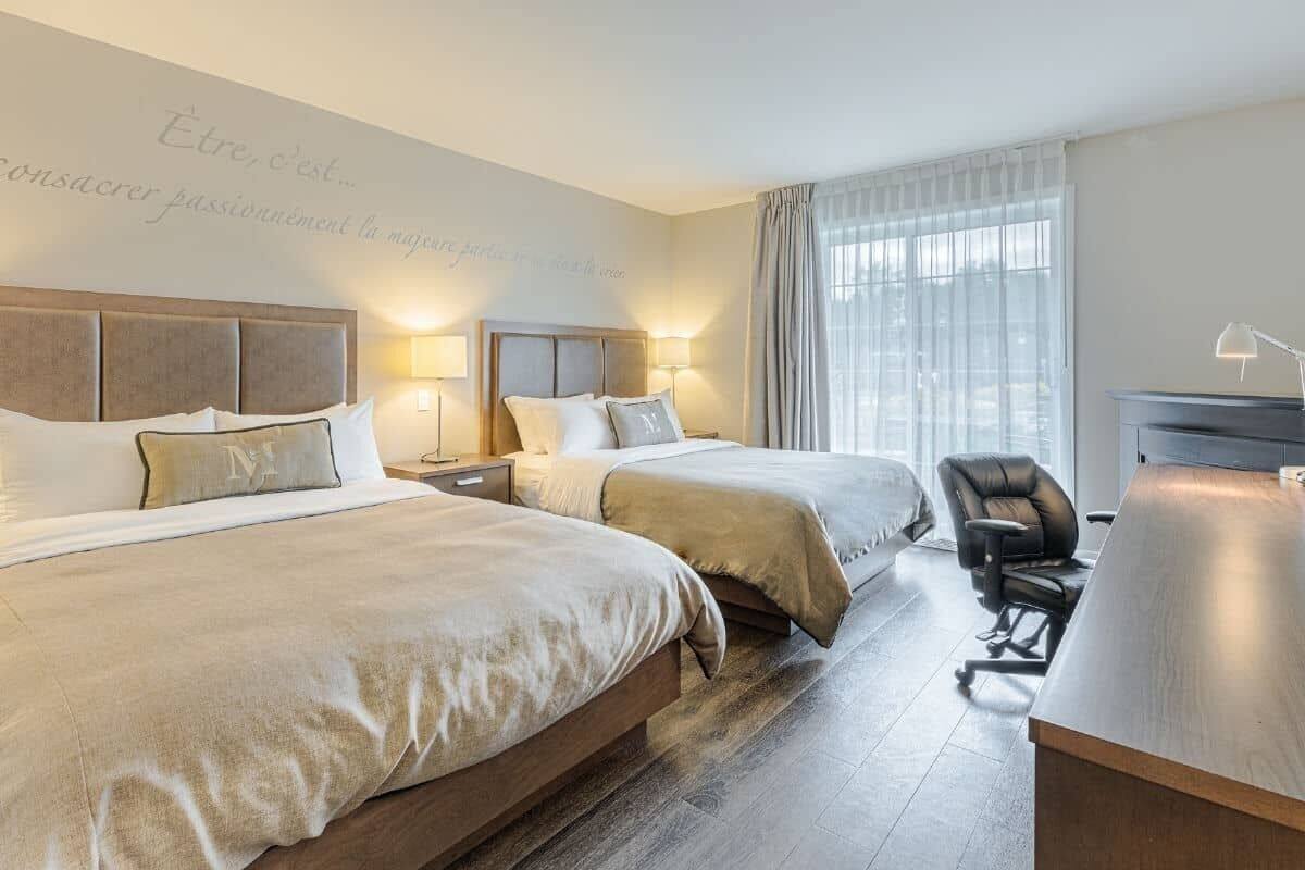 A hotel room with two beds, a desk, and a chair.