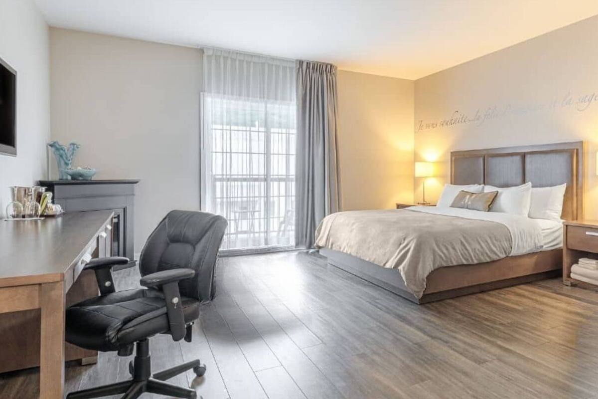 A hotel room with a bed, desk, chair, and a TV on the wall.