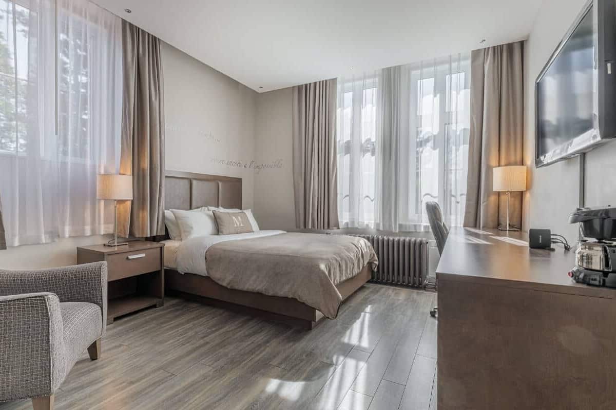 A modern hotel room with a large bed, a desk with a coffee maker, a chair, and a TV.