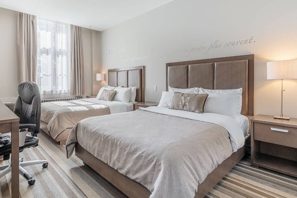 A hotel room with two beds, a desk, and a chair.