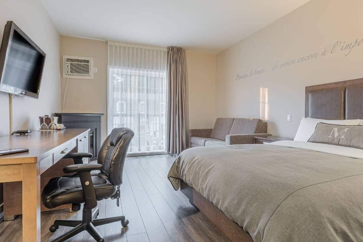 A hotel room with a bed, a desk with a chair, a television, and a window with curtains.