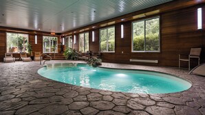 Una piscina interior con suelo de piedra, paredes de madera y grandes ventanales que ofrecen vistas al verdor.