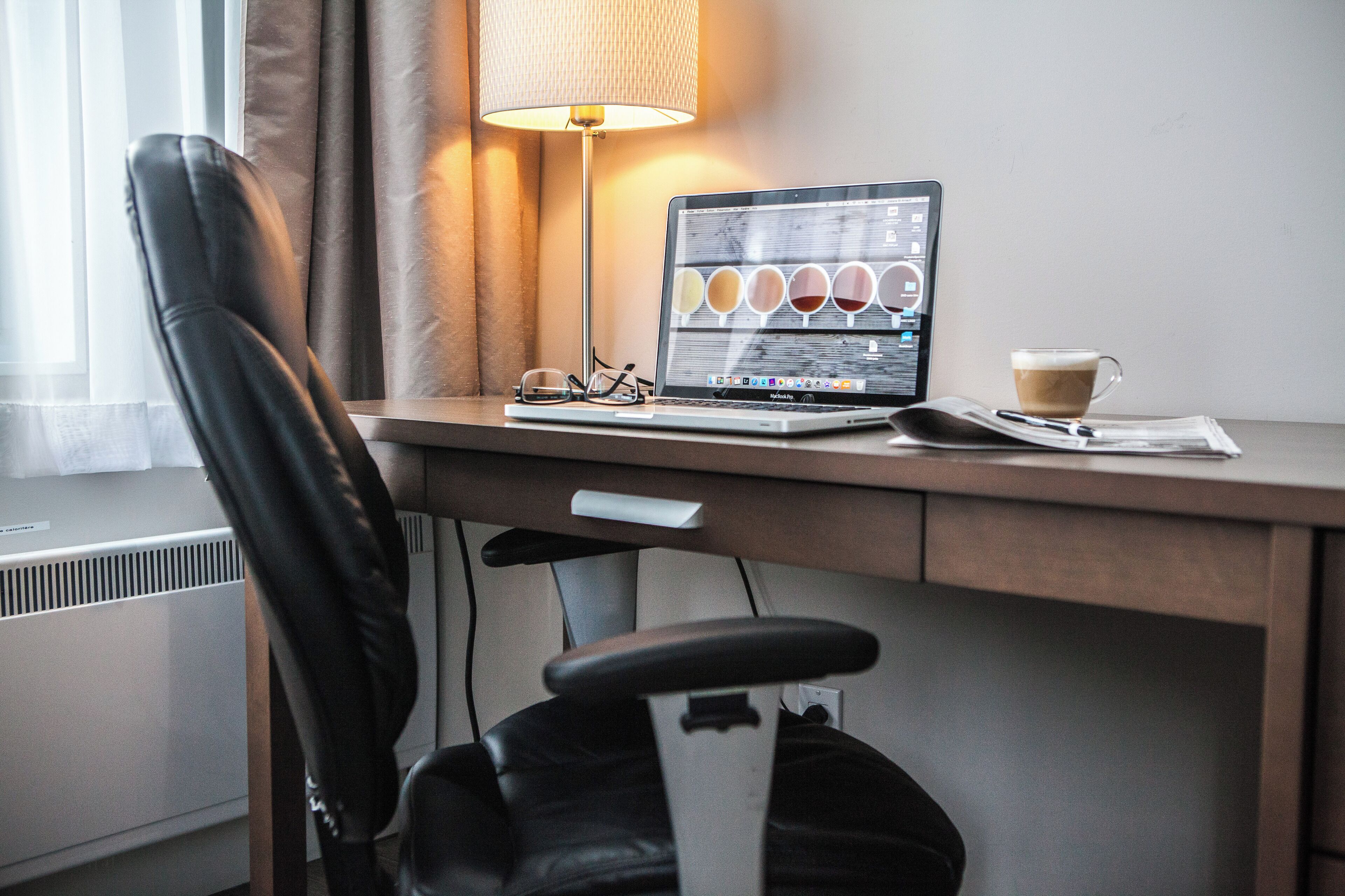 A hotel workspace with a laptop, a cup of coffee, and a pair of glasses on a desk.