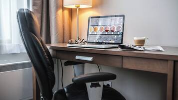 A hotel workspace with a laptop, a cup of coffee, and a pair of glasses on a desk.