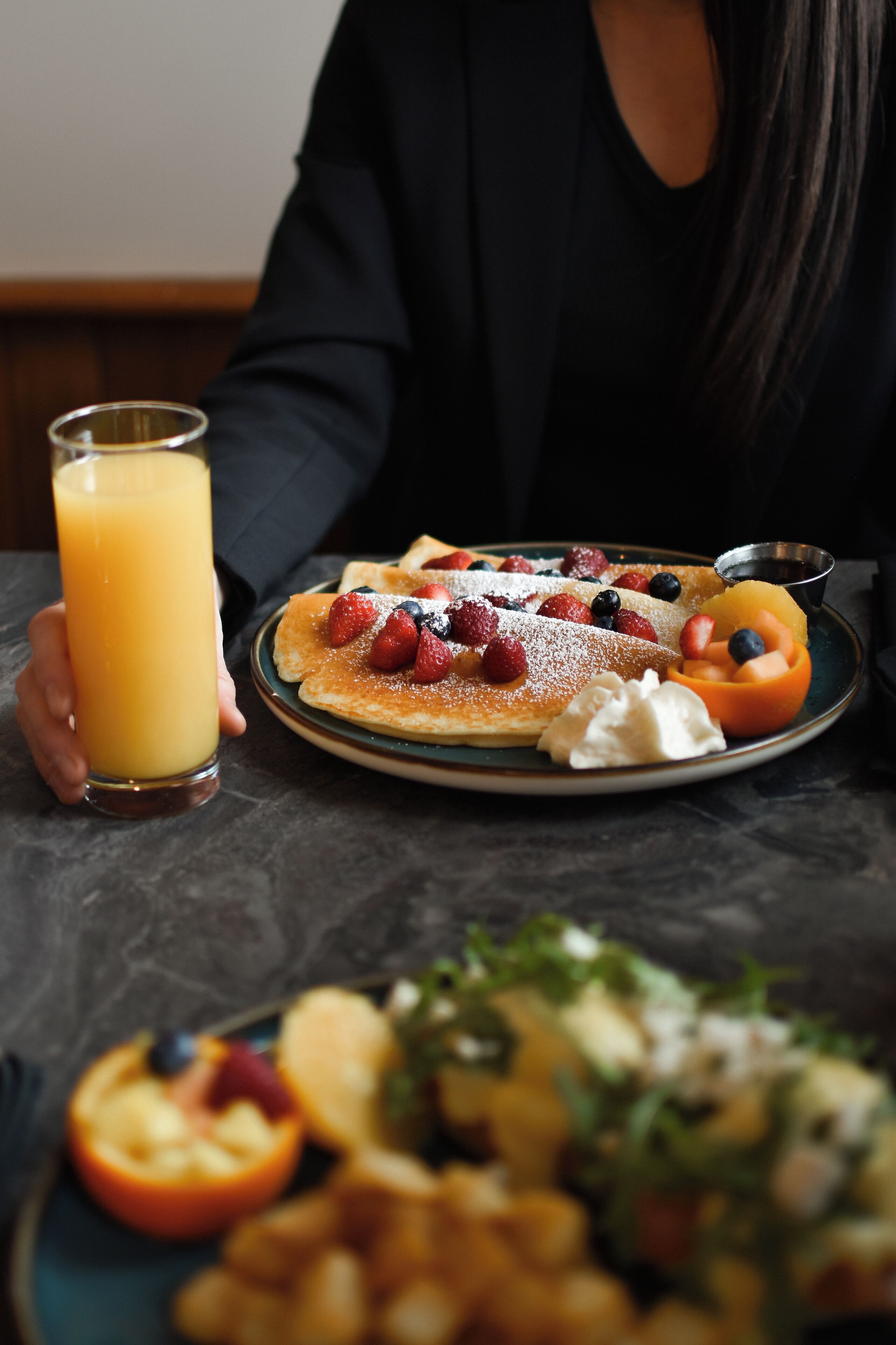 A breakfast setting with pancakes topped with berries and a glass of orange juice.