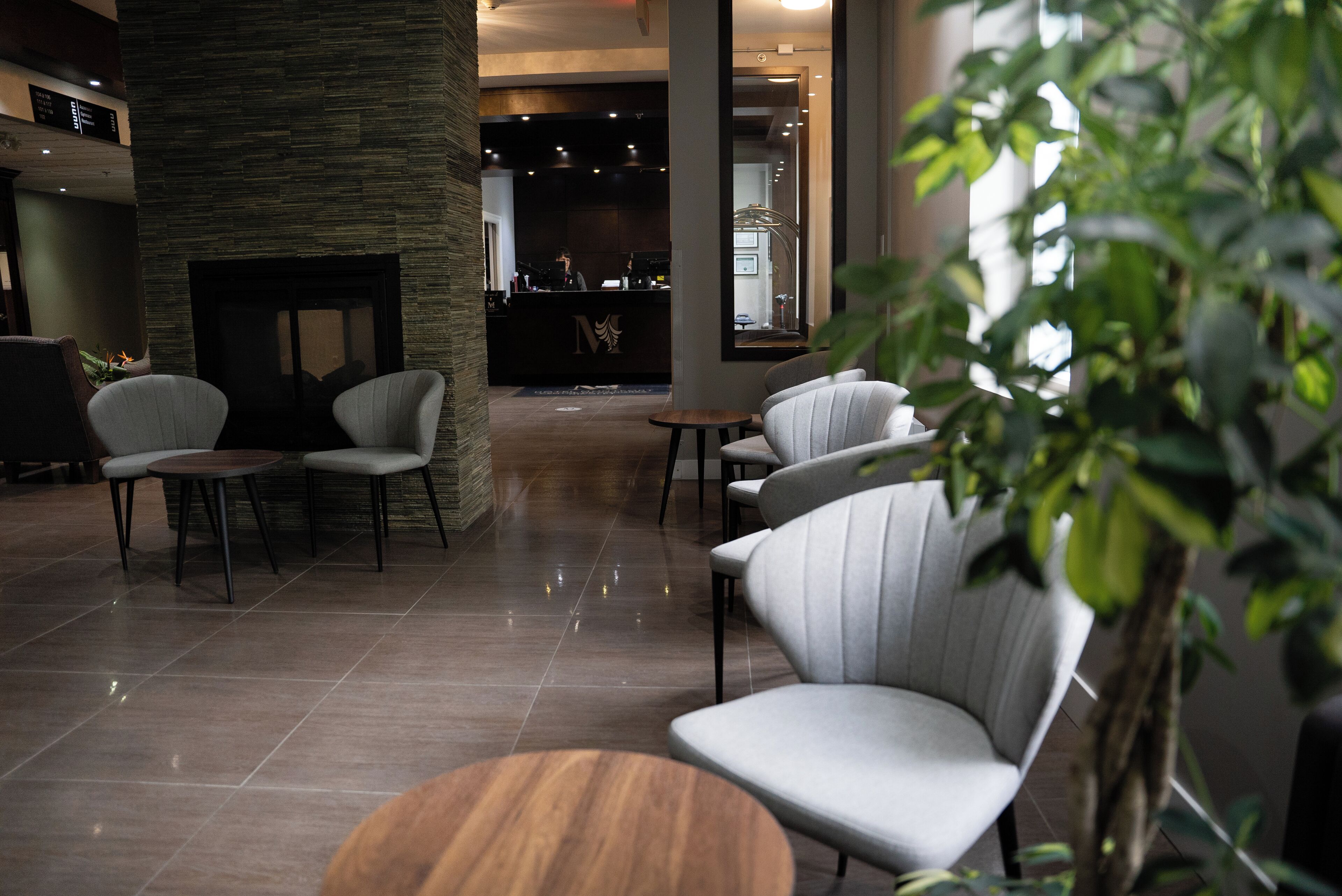 Een moderne lobby met een stenen muur, een receptiebalie en zithoeken met ronde tafels en comfortabele stoelen.