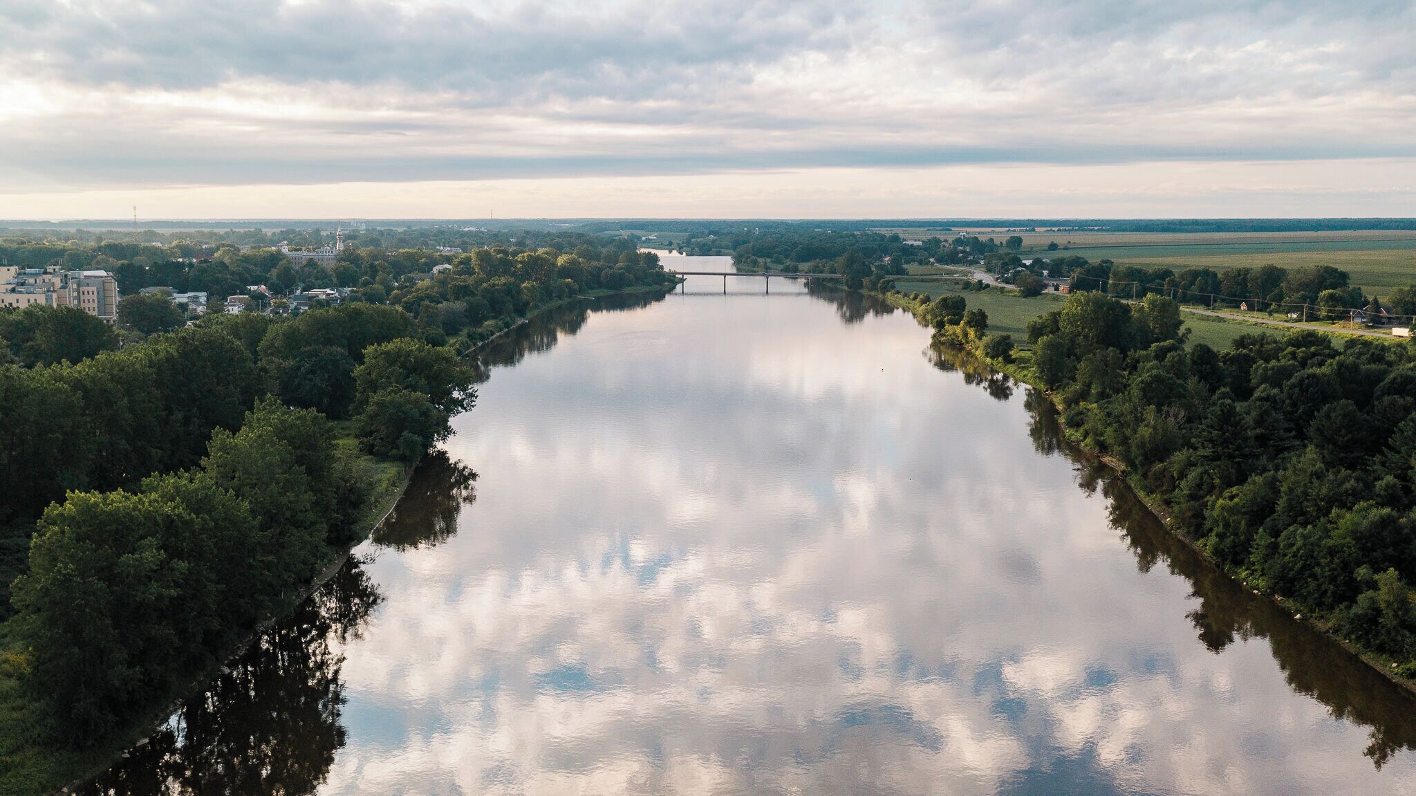 Un río flanqueado por densa vegetación y un puente a lo lejos.