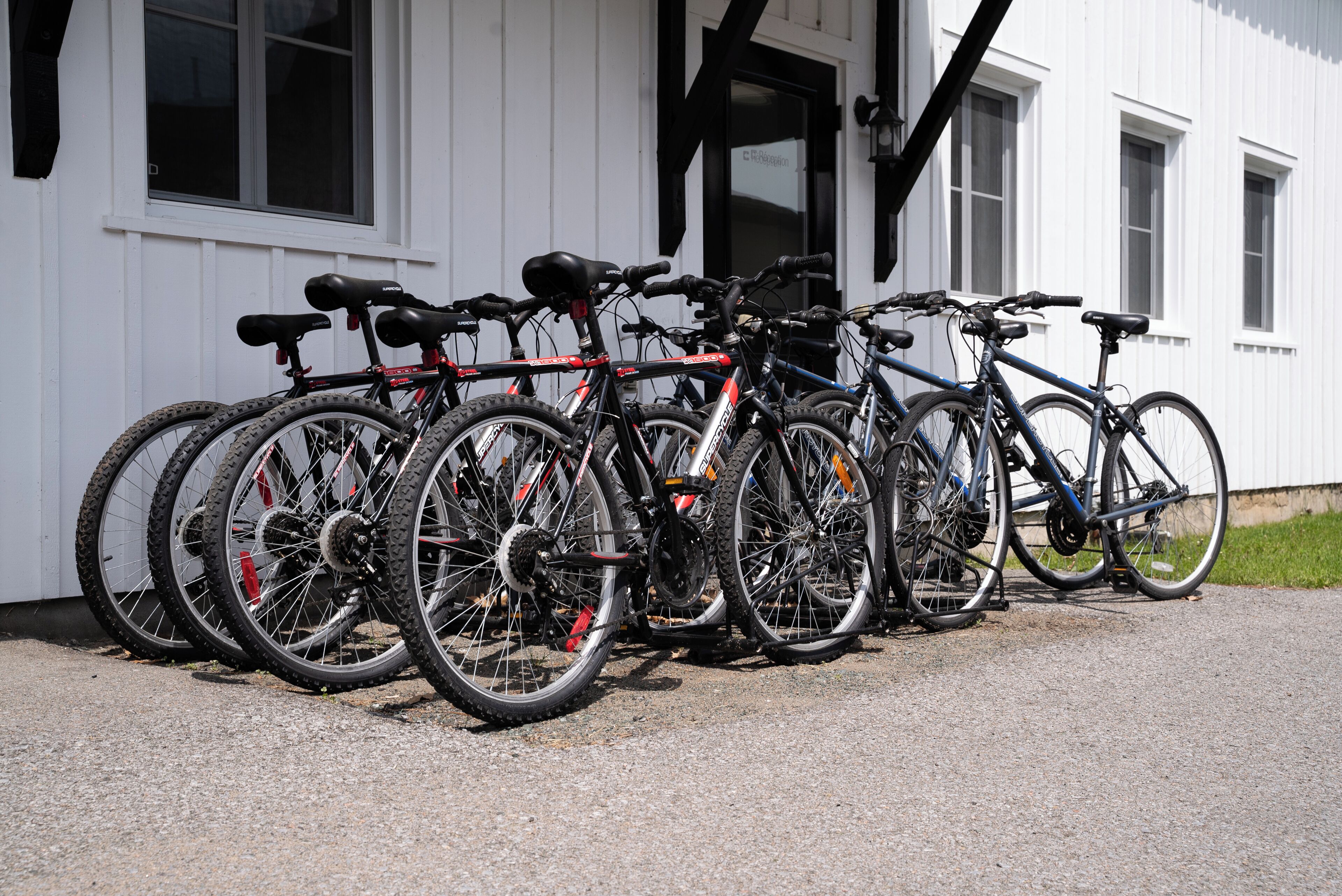 Une rangée de vélos est garée devant un bâtiment aux murs blancs et aux fenêtres à cadre noir.