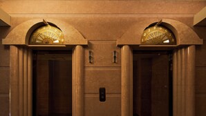 Un ascenseur surmonté de deux grandes horloges arquées de couleur dorée, placées au-dessus des portes.