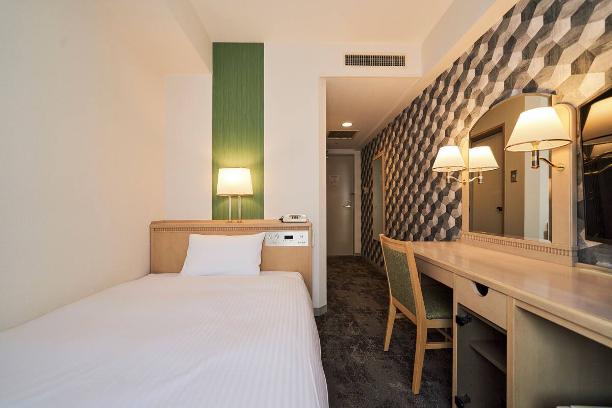 Ein Hotelzimmer mit Bett, Schreibtisch, Stuhl und Spiegel.