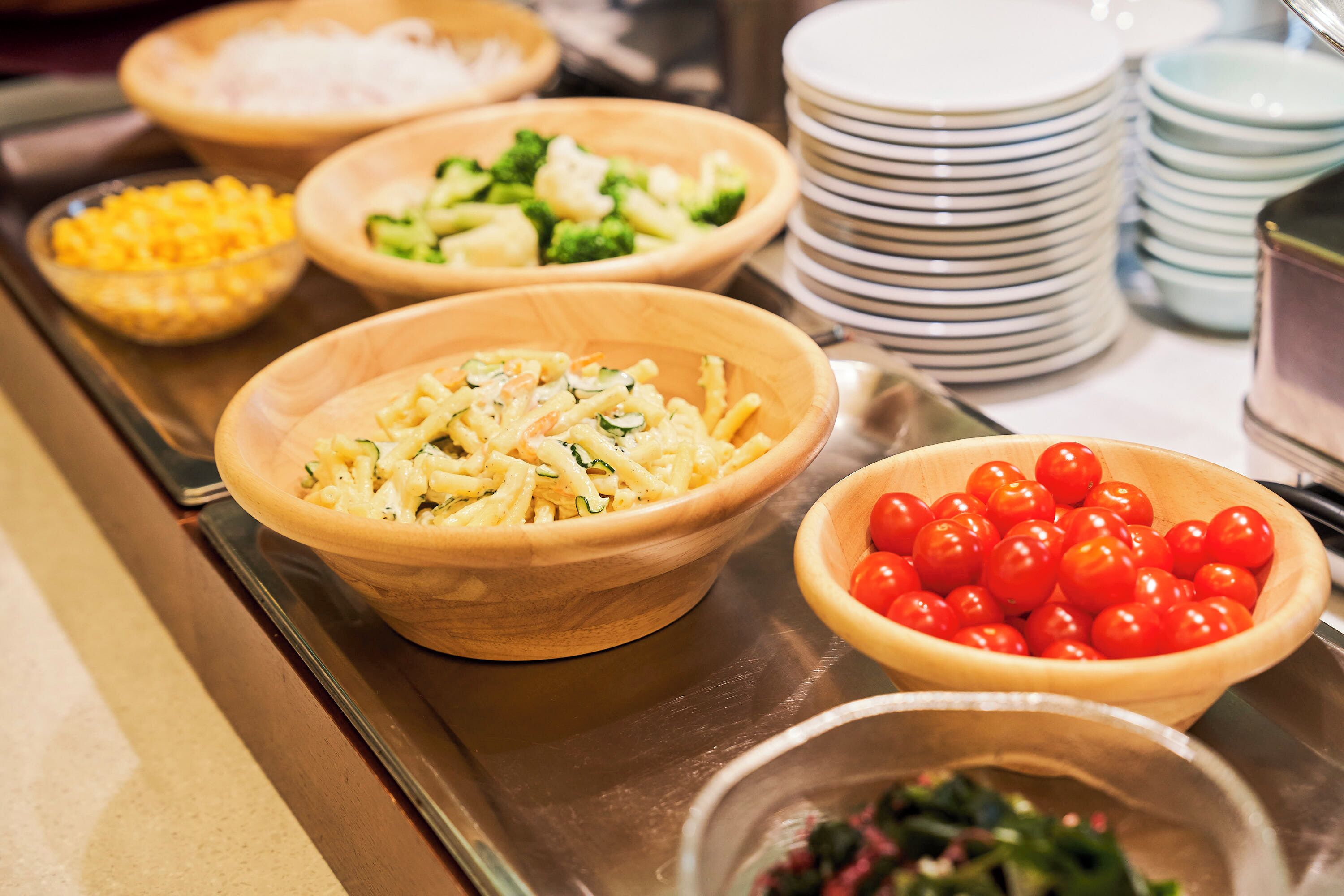 A buffet with various dishes including pasta, broccoli, and cherry tomatoes.
