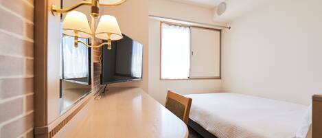 Habitación de hotel con escritorio de madera, una silla, una cama, un espejo grande y una ventana con cortinas.