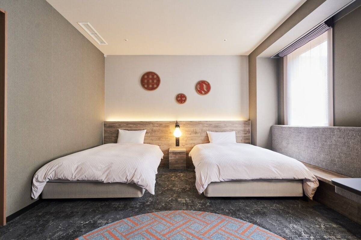 Ein Hotelzimmer mit zwei Betten, einem runden Teppich, einer Wandleuchte und zwei Wandbildern.