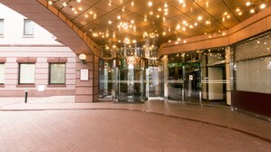 L’entrée d’un hôtel, avec une porte tournante en verre, une façade en briques et un plafond orné de nombreuses lumières.