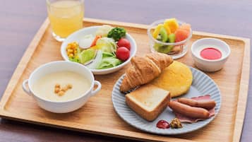 A breakfast tray with croissants, ham, toast, soup, salad, fruit, and a glass of juice.