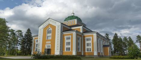 A church with a green dome and yellow walls, surrounded by trees and a grassy area.