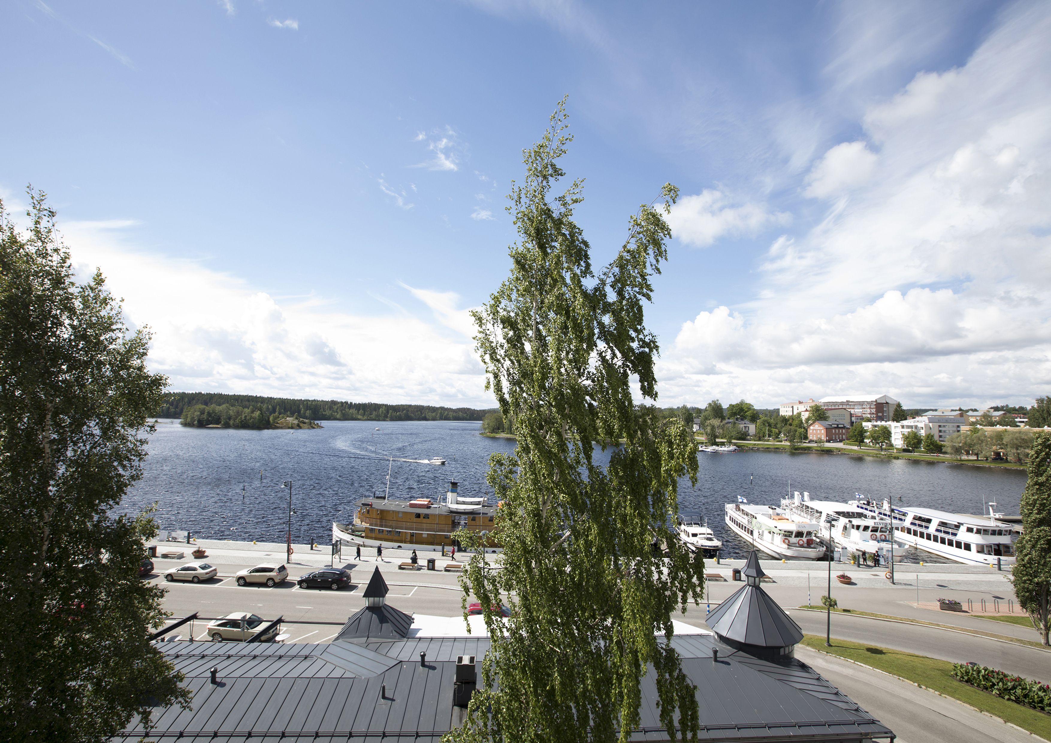 A waterfront view with a large white cruise ship docked, a building with a distinctive roof, and a calm river.