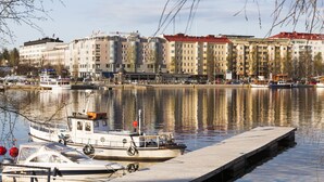 Une vue sur le front de mer, avec un bateau amarré, des bâtiments aux toits rouges et une rivière paisible qui reflète les structures environnantes.