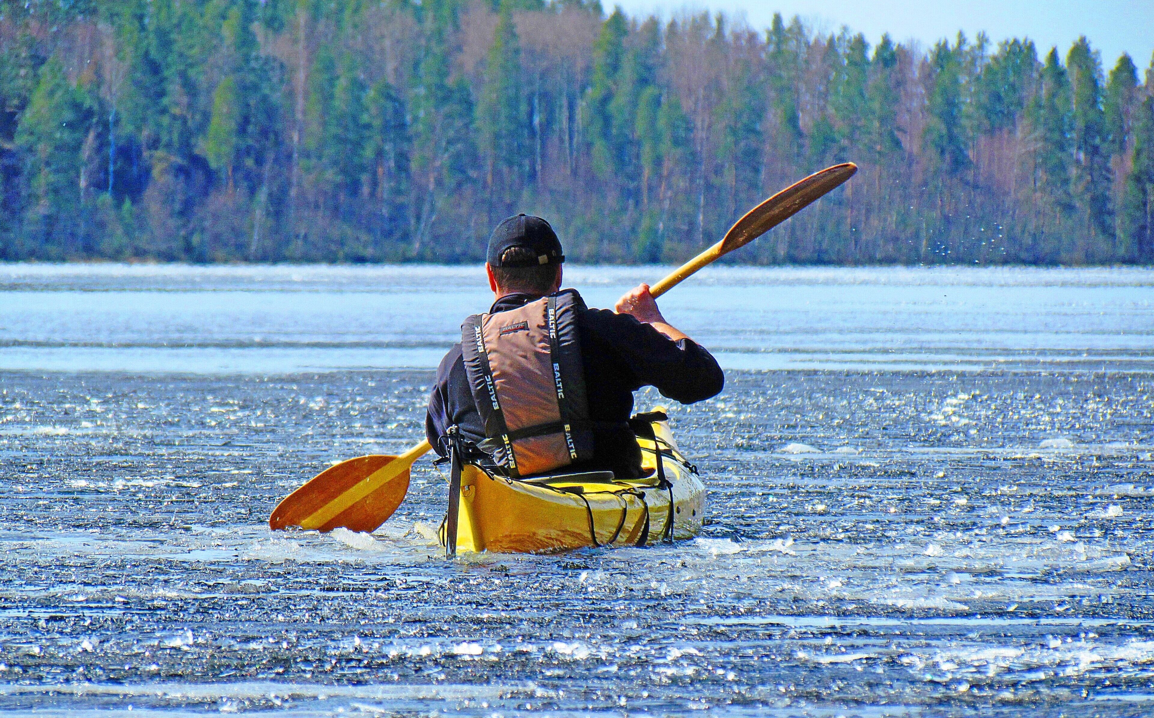 Una persona en kayak sobre un lago helado, con un bosque al fondo.