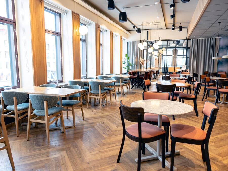 Un'ampia sala ristorante con soffitti alti, ampie finestre e diversi tipi di posti a sedere, tra cui tavoli e sedie.