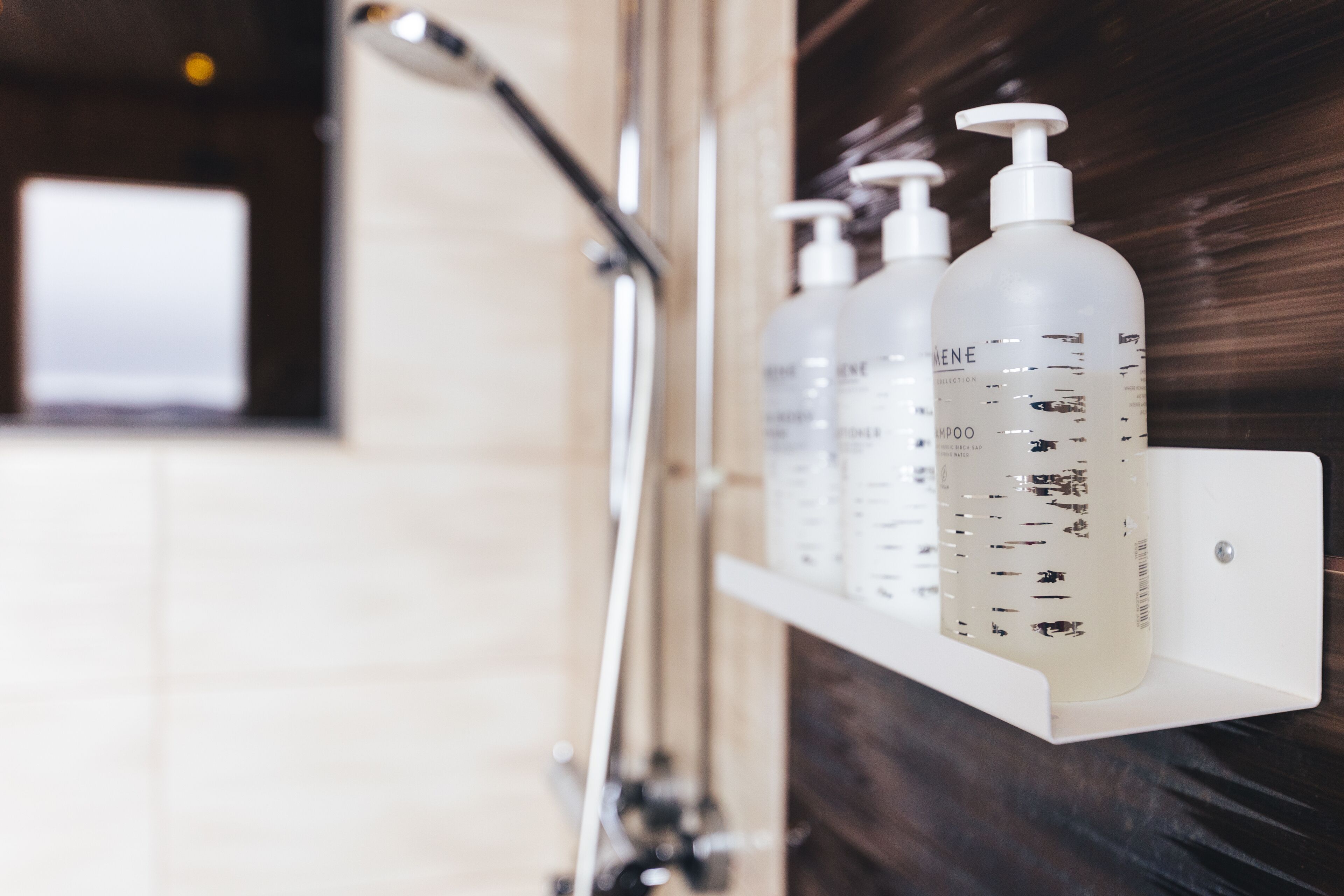Une salle de bain avec une étagère blanche sur laquelle sont posées trois bouteilles de shampoing.