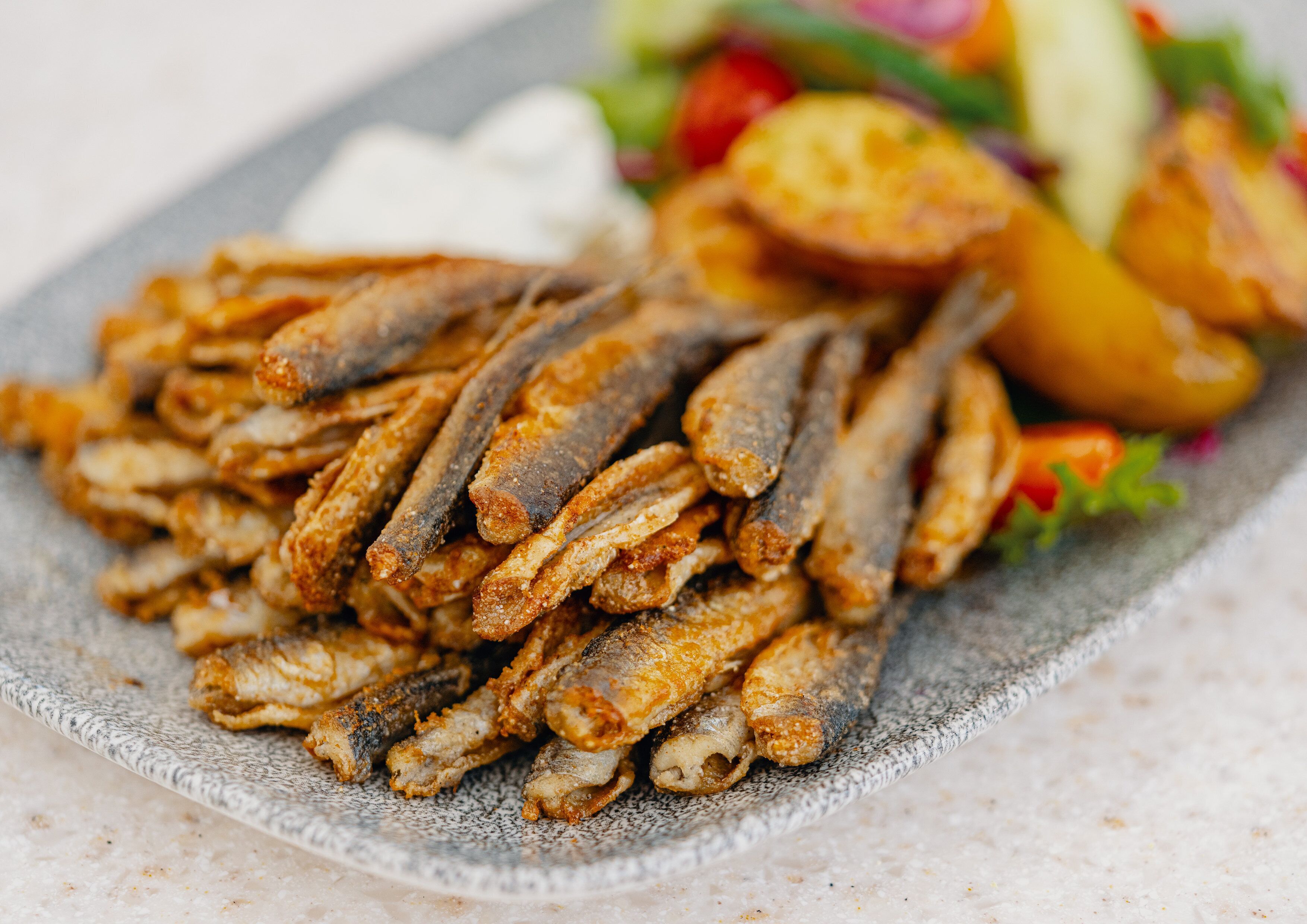 A plate of fried fish with a side salad and roasted potatoes.