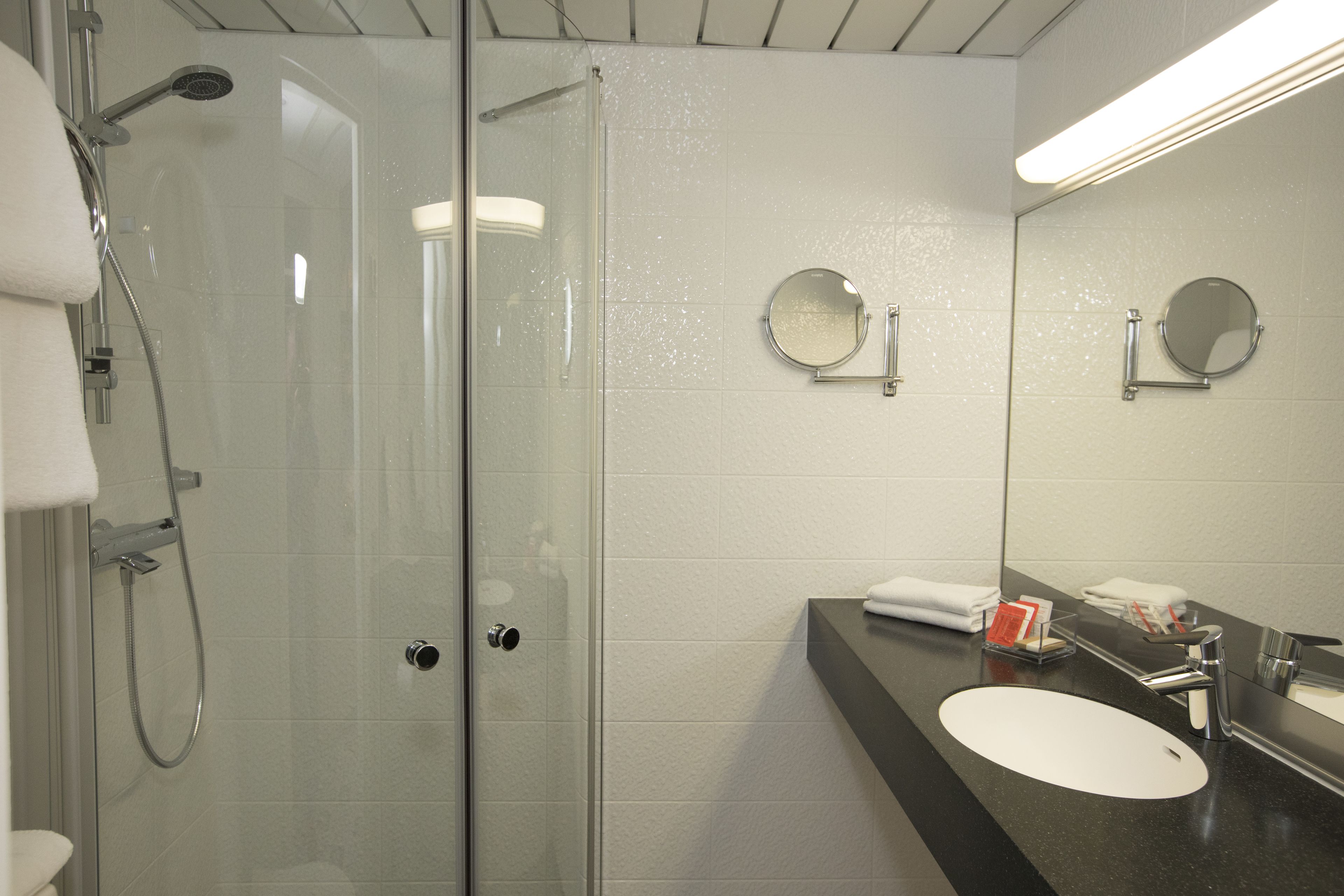 Un baño moderno con ducha envuelta en vidrio, un lavabo con espejo y un perchero para toallas.