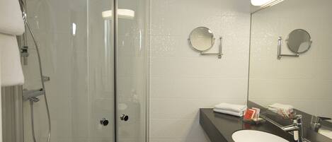 Un baño moderno con ducha envuelta en vidrio, un lavabo con espejo y un perchero para toallas.